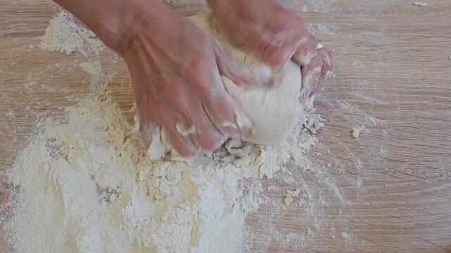Hands kneading dough on floured wooden surface during homemade bread preparation