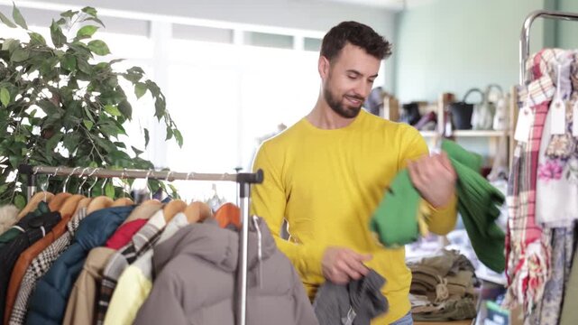 Undecided young man looking for warm pullover in retail outlet with new winter collection
