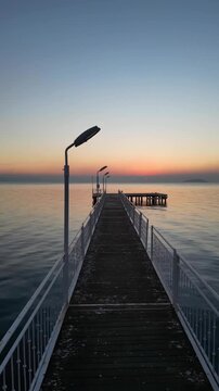 First-person perspective of a wooden jetty leading to the ocean during a beautiful golden sunrise.