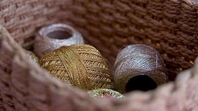 Close Up Of Golden And Silver Decorative Thread Spools In Wicker Basket