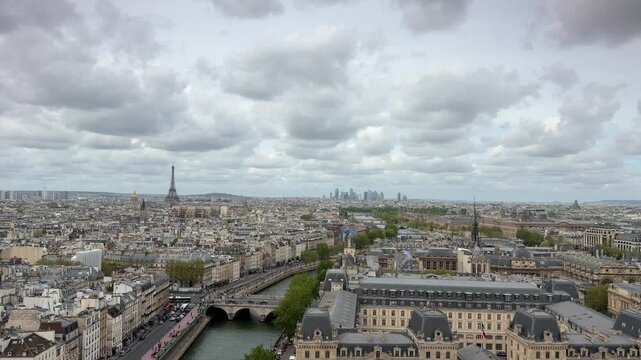 High-angle view of the Paris cityscape showing the Eiffel Tower, the financial district of La D&eacute;fense, and the Seine river on an overcast day with fast-moving clouds and urban traffic