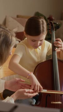 Vertical video of Caucasian child girl practicing cello with teacher guiding her hand. Footage is ideal for marketing music schools, private tutoring, and creative arts education