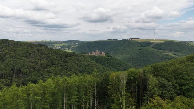 Beautiful aerial view flying towards the medieval bourscheid castle, nestled in the lush green hills and dense forests of the luxembourg ardennes region on a cloudy summer day