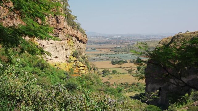 Pan right view of canyon cliffs, vegetation, and distant agricultural fields in Guanajuato at La Garita Canyon, Sierra Penjamo