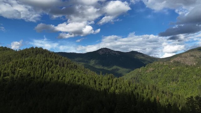 Aerial of forested mountain in Shoshone County Idaho near Wardner Peak in spring featuring dense evergreen trees under a partly cloudy sky