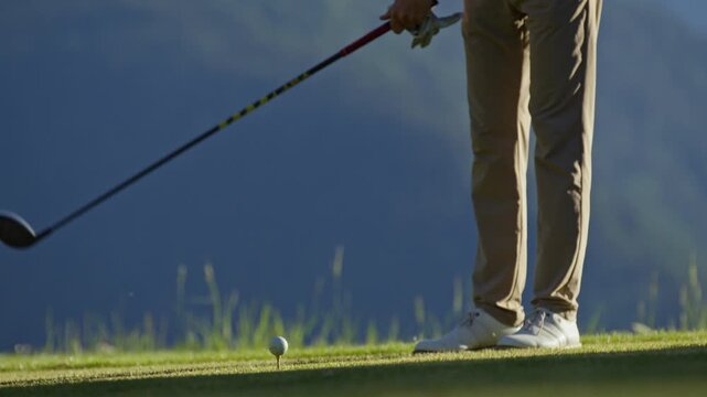 Low-angle view of a golfer performing a practice swing beside a teed golf ball on an alpine course in Verbier, Switzerland. Training, preparation and golf technique in the Swiss Alps.