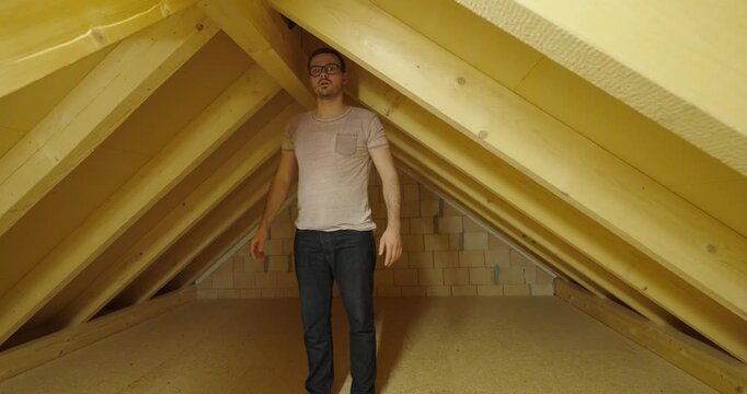 Man standing in an attic and measuring the available headroom beneath the roof structure.