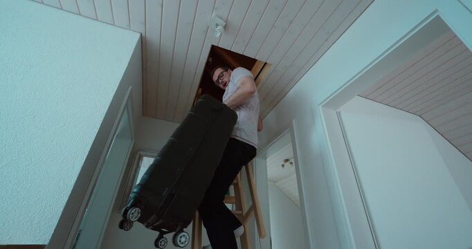 Person lifting a heavy suitcase through an attic hatch to store it in the loft. Suitable for storage, moving, home organization, attic access, and household safety concepts.