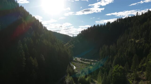 Aerial of forested valley in Shoshone County Idaho with dense evergreen trees and a winding road under cloudy skies at sunset in spring