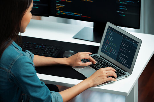 Smiling young Asian in IT developer creating with typing online information on laptop with coding program data of application, wearing jeans shirt. surrounded by safety analysis two screen. Stratagem.