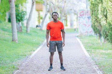 Obraz premium Athlete standing on a park path, listening to music and wearing a smartphone armband