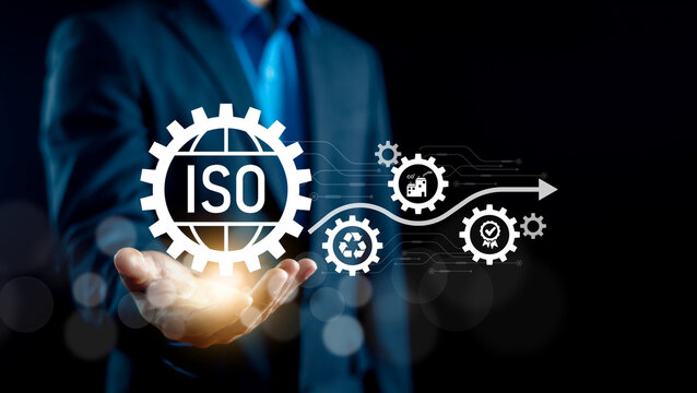 Professional businessman hand holding virtual ISO certification icon with industrial gear flow and environmental compliance symbols. Concept of quality management, and manufacturing standards.