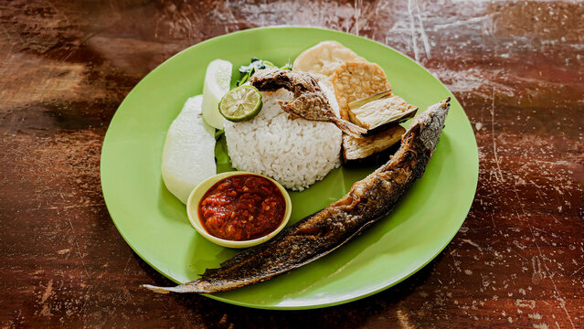 Pecel Lele Indonesian Fried Catfish served with Rice Tempeh Tofu Sambal and Vegetables on Green Plate