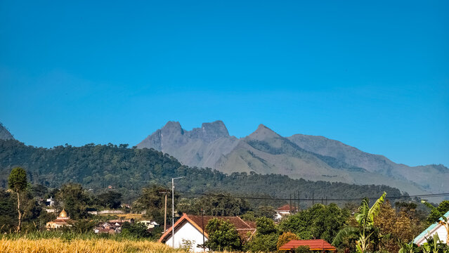 Majestic volcanic mountain peaks rising above a lush tropical rural village under a clear bright blue sky in Indonesia