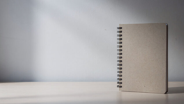 Single closed spiral notebook with kraft paper cover standing vertically on white surface against plain light background