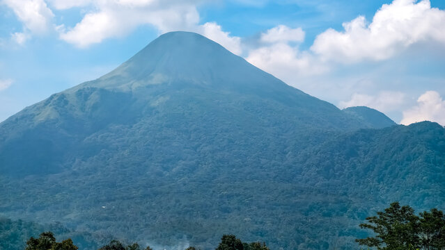 A Majestic Cone-Shaped Volcano Peak Rising Under a Bright Blue Sky with Fluffy White Clouds in a Lush Green Landscape