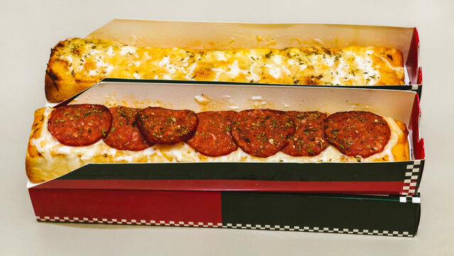 Two pepperoni and cheese garlic bread pizzas in takeout boxes