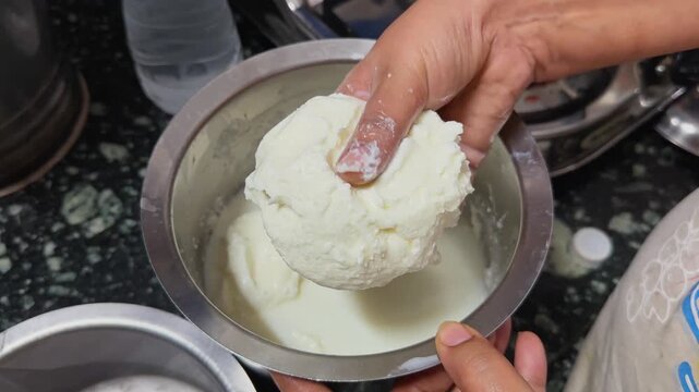 Hand transferring freshly churned white butter from buttermilk into a metal utensil showcasing traditional dairy processing and homemade butter preparation.