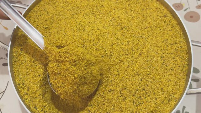 Closeup view of traditional Indian mango pickle masala being scooped with a metal ladle revealing the coarse texture of mustard and fenugreek spice blend used in homemade achar preparation