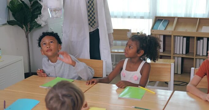 Happy elementary students reach out to touch dry ice smoke from a beaker held by their science teacher.