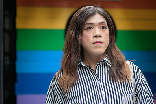 Thai Isan transgender woman in 40s looking aside against rainbow pride background