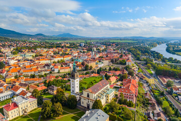 A drone captures a stunning aerial view of St. Stephen's Cathedral surrounded by historic buildings in Litomerice, Czechia. The vibrant architecture contrasts with green landscapes.