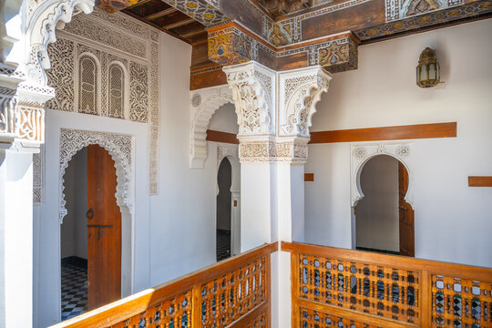 Student rooms at Madrasa Ben Youssef show traditional Moroccan architecture. The wooden balcony overlooks a courtyard. The space has intricate designs and small doorways leading to different rooms.