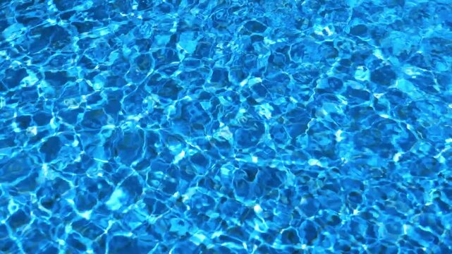 Rippling blue water surface in swimming pool with sun light reflections creating abstract patterns.