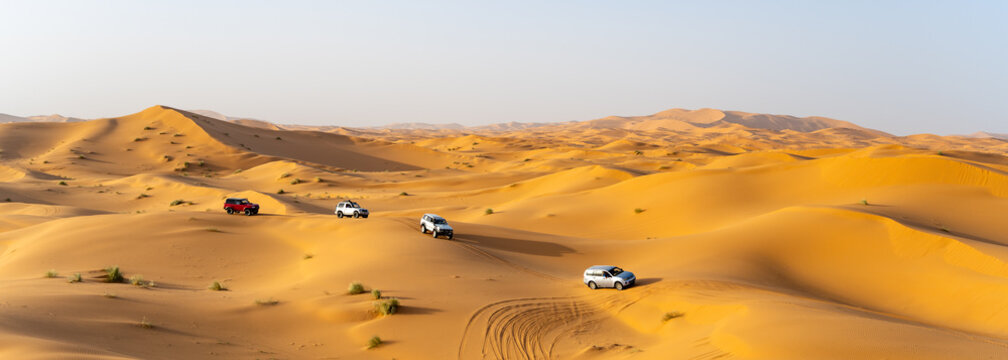 Off-road vehicles move across the sandy terrain of the Sahara in Morocco. The sun shines brightly as the vehicles create tracks in the soft sand.