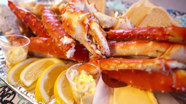 Fresh king crab legs served with lemon wedges and melted butter sauce on a silver platter.