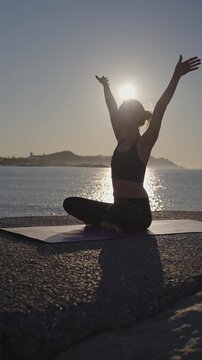A person practices yoga on the beach. The sun rises, creating a glow behind them. The ocean waves gently lap at the shore. This is a time for focus and stretching.