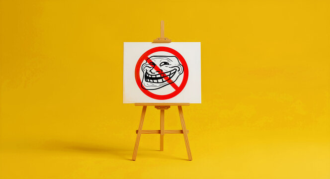 No trolling sign on a canvas displayed on a wooden easel against a yellow background. Anti-harassment symbol featuring a banned meme face. Internet safety and social media moderation concept.