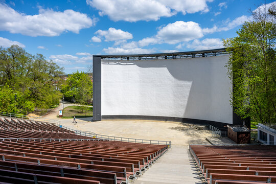 At Boskovice, Czechia, a summer cinema hosts outdoor movie screenings. The large screen stands ready for films, surrounded by rows of empty seats and green trees under a blue sky.