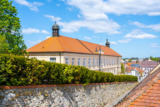The view shows the former monastery of St. Vincent de Paul in Boskovice, Czechia. This location features historic architecture and is surrounded by trees and a stone wall under a bright sky.
