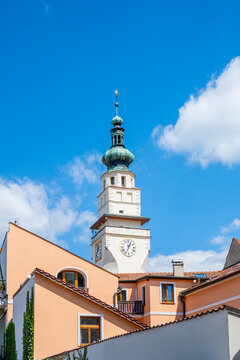 The town hall tower in Boskovice is visible against a blue sky. White clouds drift in the background. Buildings surround the tower, highlighting local architecture and history in this Czech town.