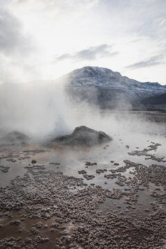 Steaming geyser erupts with snow capped mountains