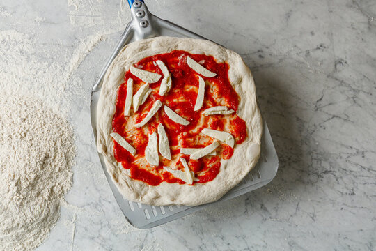 Pizza maker placing pizza on a spatula for baking in the oven