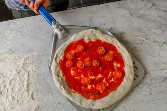 Pizza maker placing pizza on a spatula for baking in the oven