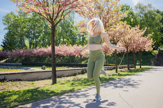 Blonde middleaged sporty woman jumping rope in spring sunny city park