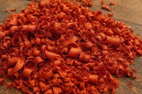 Curly, orange-red wood shavings from padauk piled on a workshop floor.