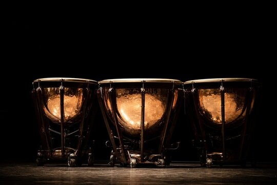 Three timpani drums with polished copper bowls reflecting light on a dark stage.