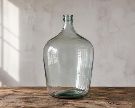 Large glass carboy on rustic wood table, home brewing storage concept.