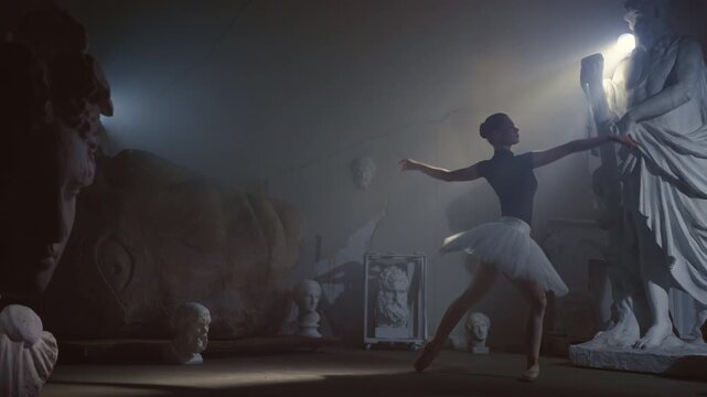 Amazing classic choreography in dark museum, festival of classical arts. Beautiful ballerina dancing, enjoying music and emotions, graceful female silhouette between statues of Greek gods in museum