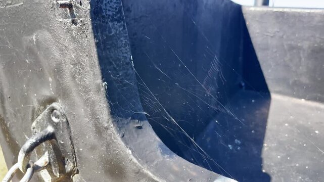 Cobwebs fluttering in the wind inside an old outboard motor. Detailed footage of spider silk catching the light on aged boating equipment.