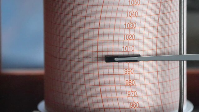 Mechanical vessel barometer recorder measuring atmospheric pressure during a sea voyage through the Drake Passage. Close-up of instrument dial tracking weather changes in the Southern Ocean.