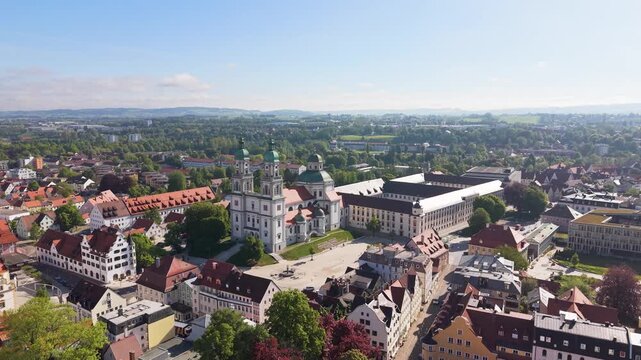 Rising drone shot of Kempten in Bavaria featuring the Basilica of Saint Lorenz surrounded by historic buildings and a green urban landscape under bright daylight, UHD.