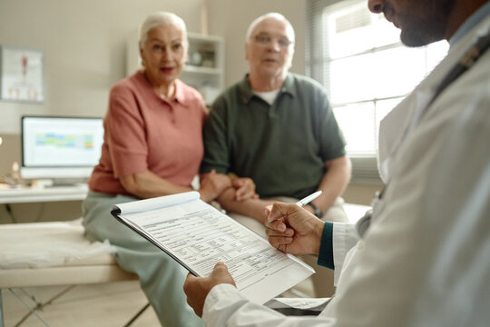Senior couple consulting doctor in clinic, reviewing medical form and discussing treatment plan. Healthcare access and preventive care concept for insurance, senior wellness, patient services