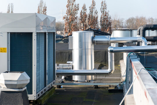 Modern industrial HVAC installation on a commercial rooftop featuring a large air conditioning unit, insulated ventilation pipes, and a stainless steel buffer tank. The image illustrates energy-effici