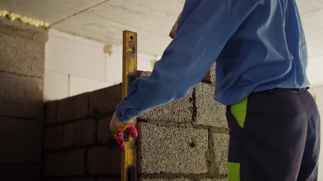 Worker checking wall alignment during concrete block installation