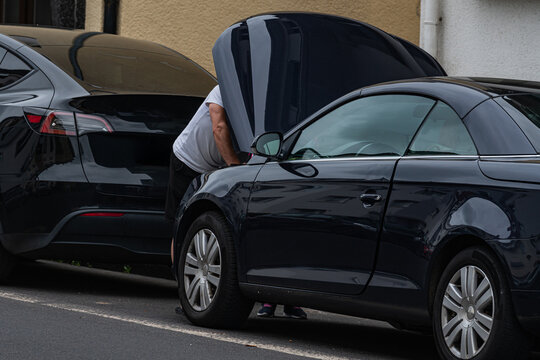 Person checks car engine in parking lot during daytime hours